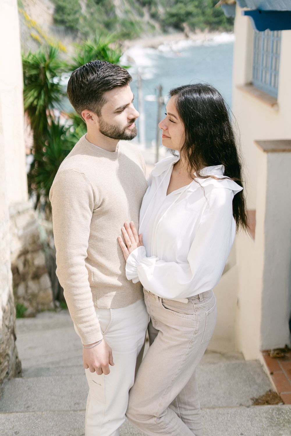 A couple in matching light colored outfits share a romantic moment on a coastal pathway overlooking the ocean.