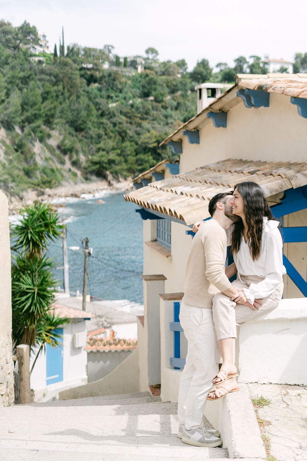Romantic seaside moment on white stairs overlooking Mediterranean coastal village with blue trim and ocean views.