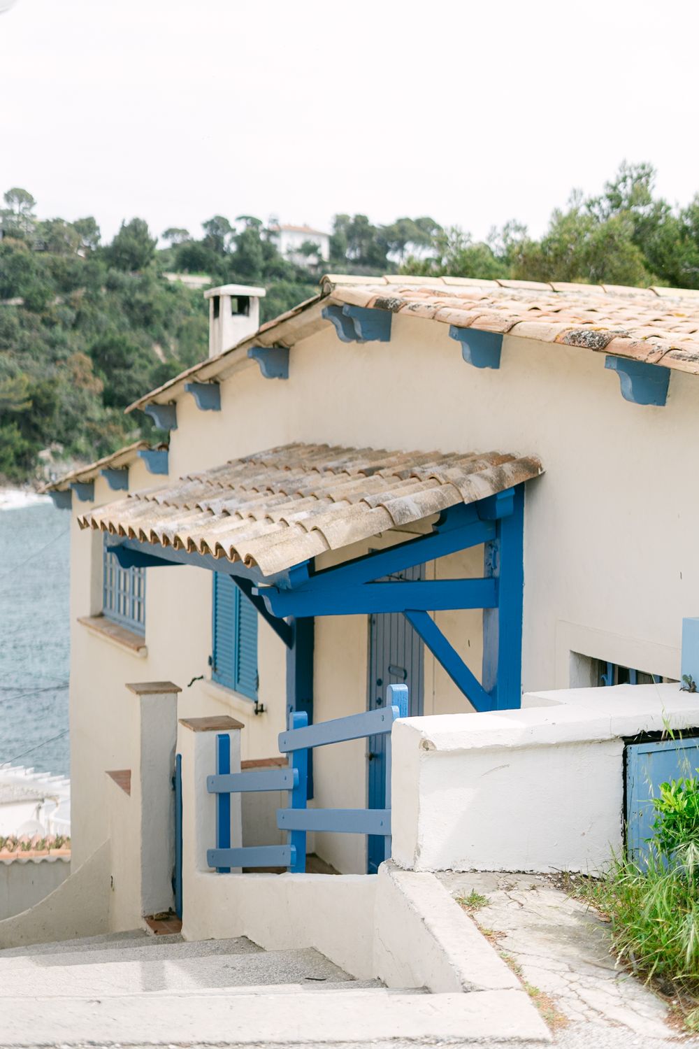 Mediterranean coastal house with white walls and bright blue trim features a curved terrace roof with terracotta tiles.