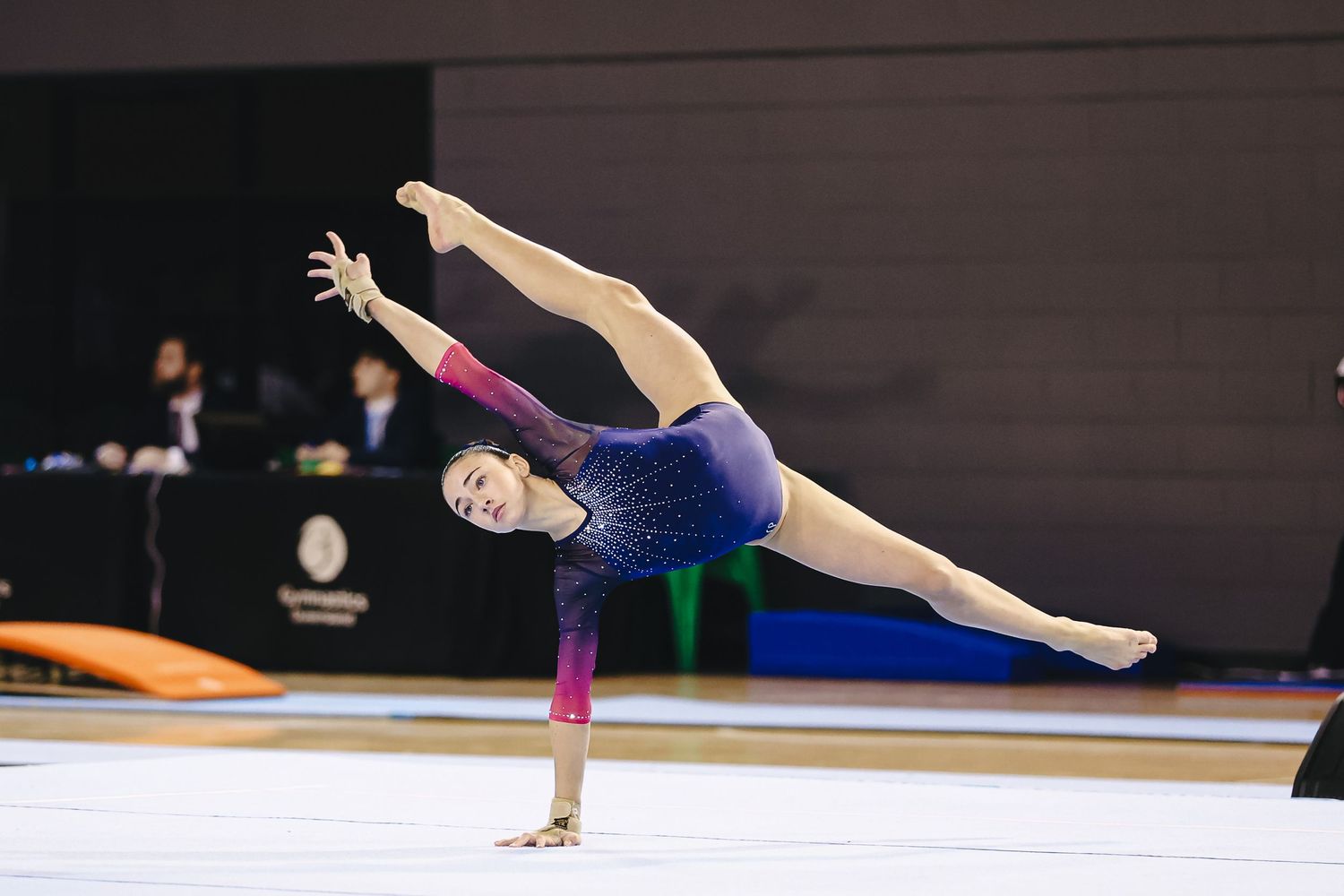 A gymnast in a purple leotard performs a skilled floor routine with a high leg extension during competition.