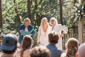 Guests gather outdoors for a sunlit forest wedding ceremony with natural decorations.