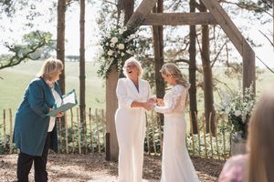A couple exchanges vows during an intimate outdoor wedding ceremony under a rustic wooden arch decorated with flowers.