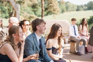 Wedding guests smile and socialize while seated outdoors during a sunny celebration on a garden patio.