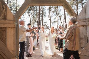 Joyful wedding celebration with guests cheering during recessional under wooden archway in forest setting.