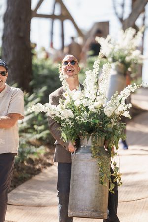A joyful moment as someone holds a large rustic metal container filled with beautiful white delphinium flowers outdoors.