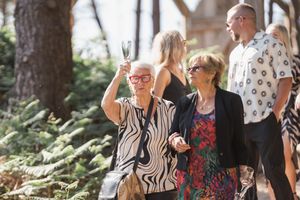 People enjoying outdoor celebration in wooded setting with drinks and casual summer attire.