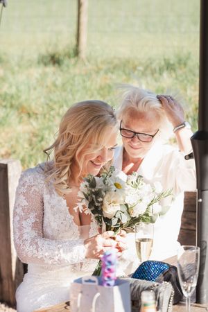 Emotional moment at wedding reception as bride in lace dress shares special moment with guest while holding white bouquet.