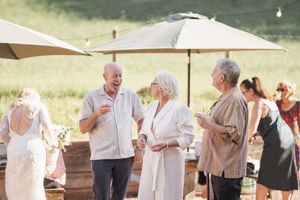 Wedding guests enjoying conversation under white umbrellas at an outdoor daytime celebration.