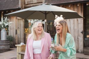Two friends in pastel blazers share a candid laughing moment together at an outdoor venue.