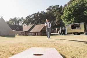 People playing cornhole at a rustic outdoor venue with tipis and wooden buildings in the background.