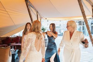 Wedding celebration under tent as bridal party dances together in elegant attire at sunset reception.