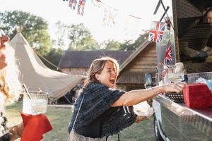 Child joyfully reaching for decorations at an outdoor party with bunting and tents.