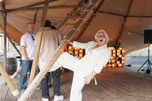 A person wearing a white dress poses playfully near a swing under a large tent with warm lighting at an event.