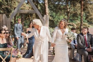 Two people sharing a joyful moment during their wedding ceremony under a rustic wooden arch in a forest setting.