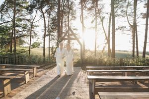Silhouetted figures stand together on wooden benches at sunset through pine trees in an outdoor setting.