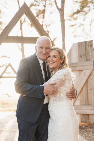 A joyful couple embraces in a sunlit forest setting during their wedding ceremony.