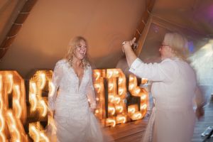 People dance together under warm glowing letter lights at a wedding reception or celebration event.