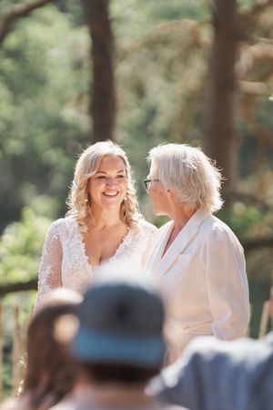 Two people share a joyful moment during an outdoor wedding ceremony in a sun-dappled forest setting.