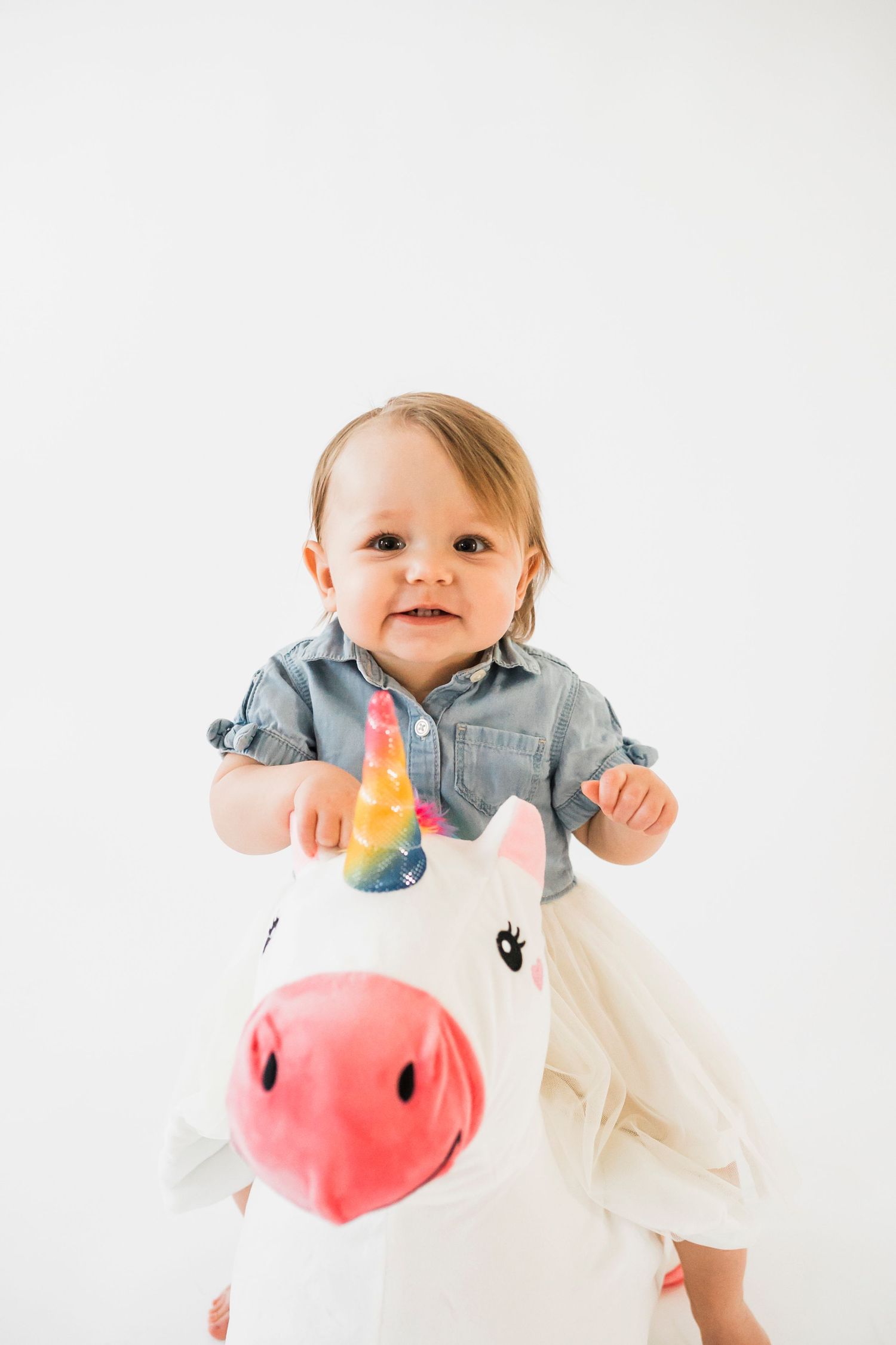 Happy family posing with plush unicorn toy against white background during studio photo shoot.