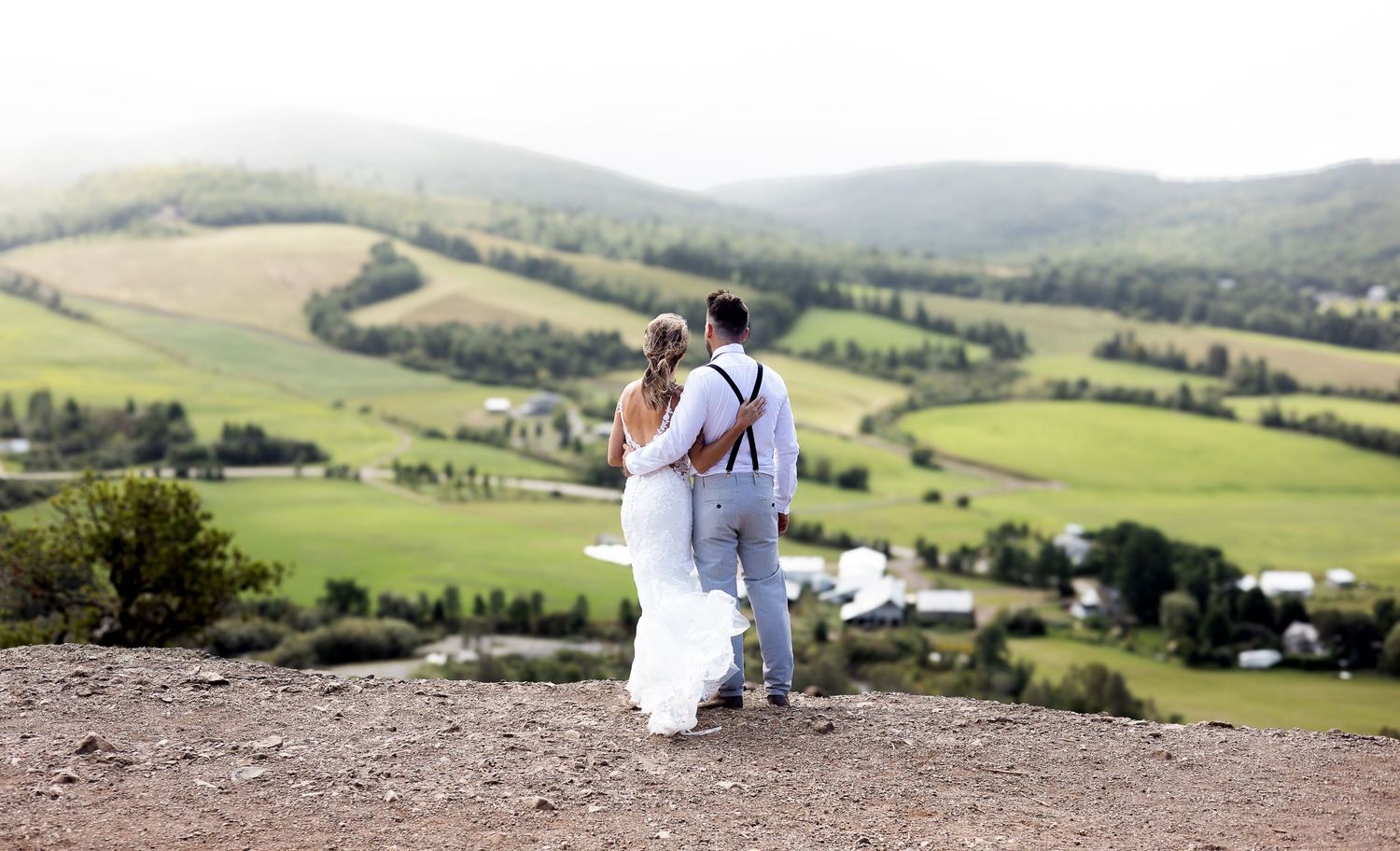 A couple walks together across a scenic hilltop with rolling countryside views.