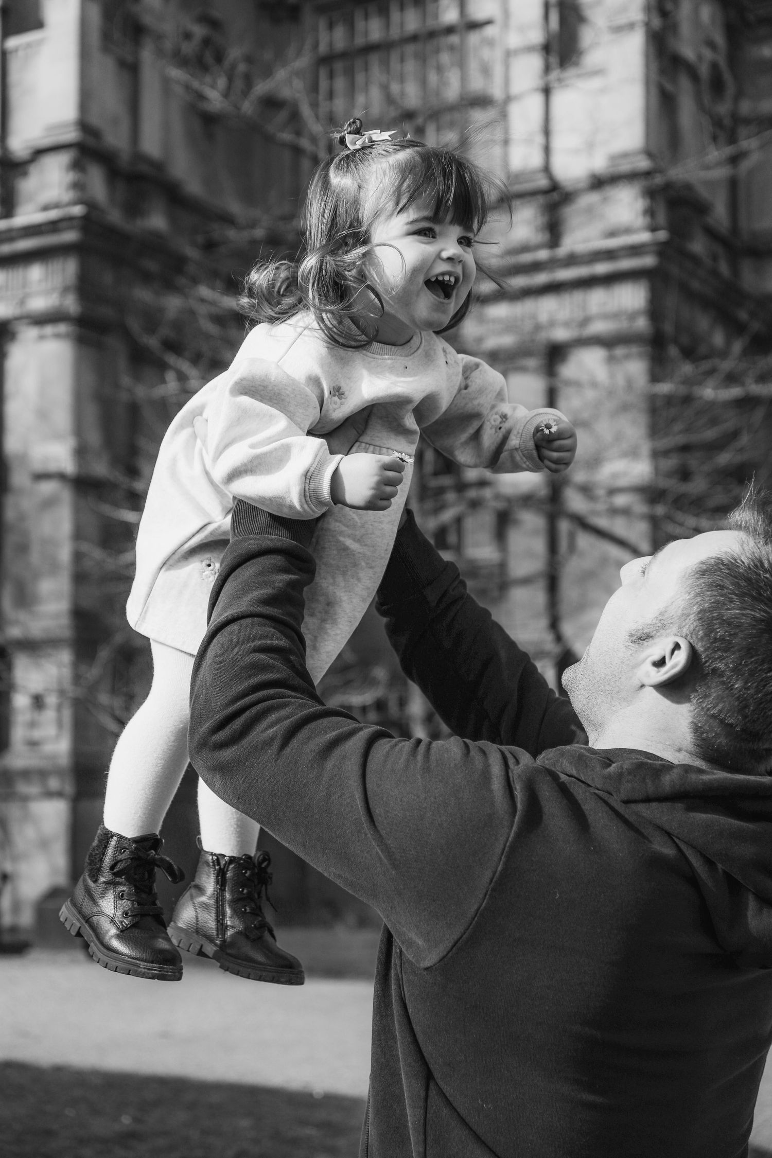 A joyful moment captured in black and white as a child is lifted high into the air outside a historic building  family shoot Nottingham