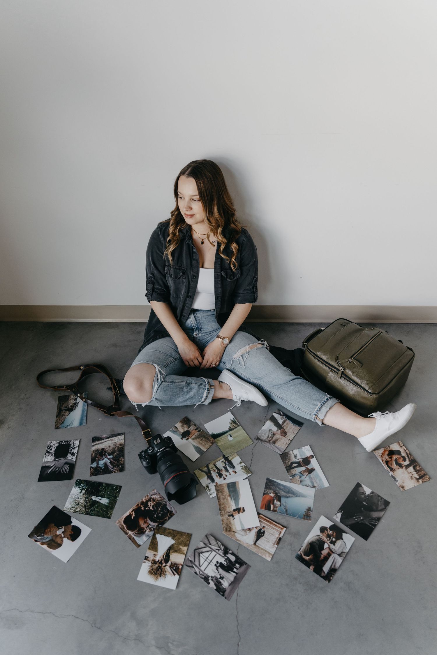 A photographer sits on the floor reviewing printed photos and camera equipment spread out around them.