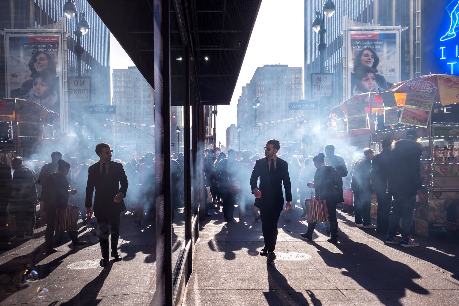 Silhouettes of people walking through smoke-filled street with neon signs in background.