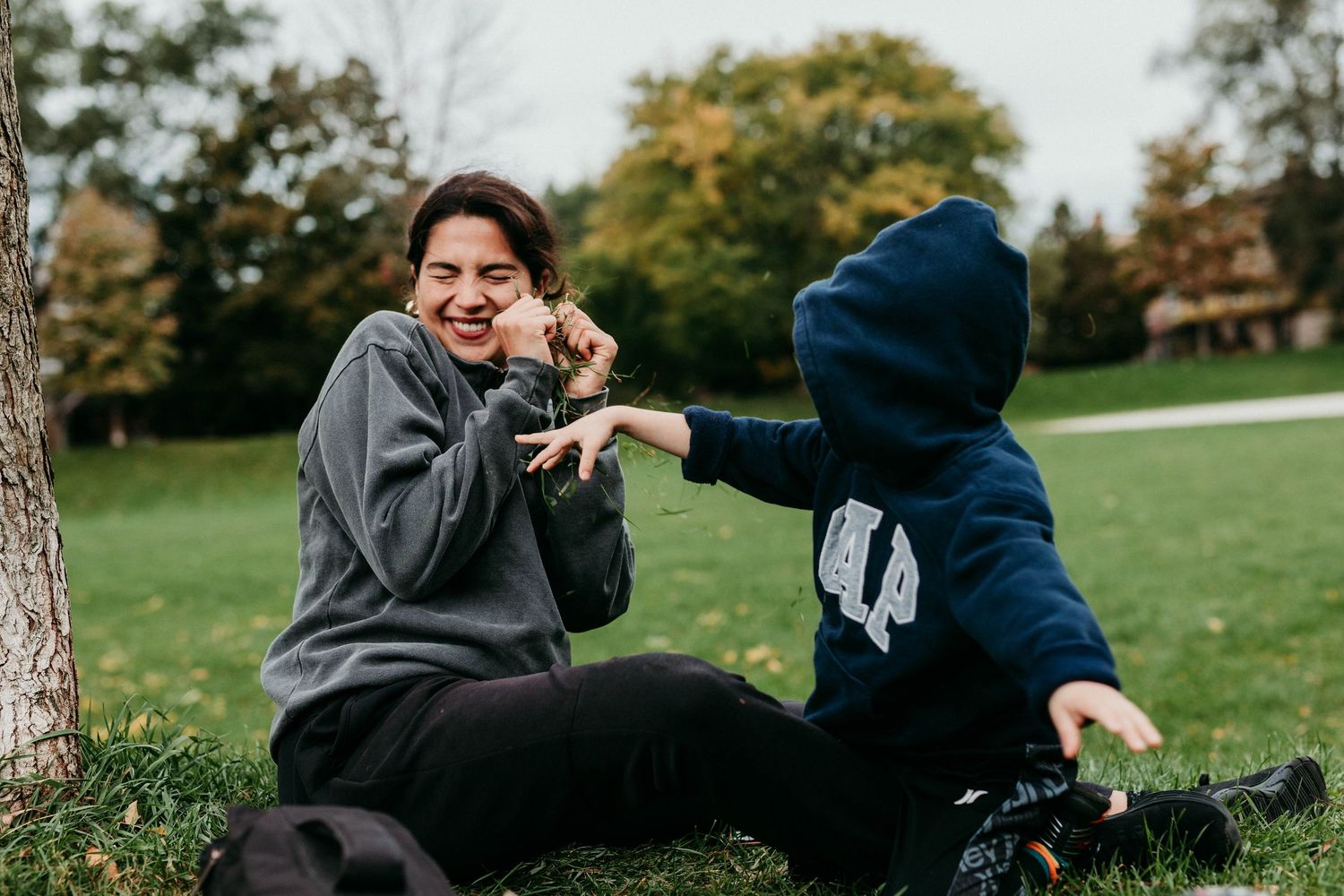 Two people playfully interact while sitting on grass in a park on an autumn day.