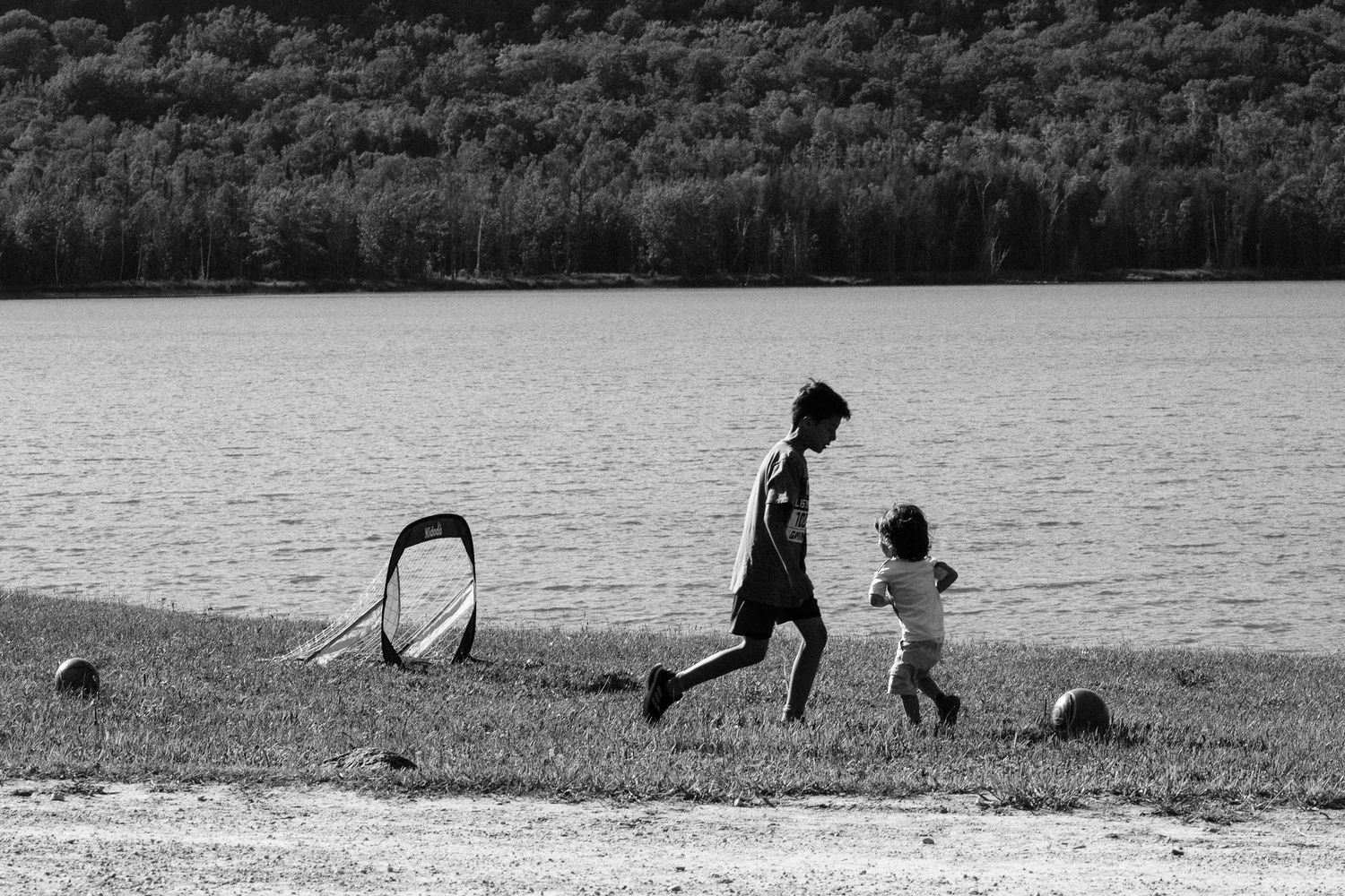 Two figures run along a lakeside beach with a hoop in the foreground, captured in black and white photography.