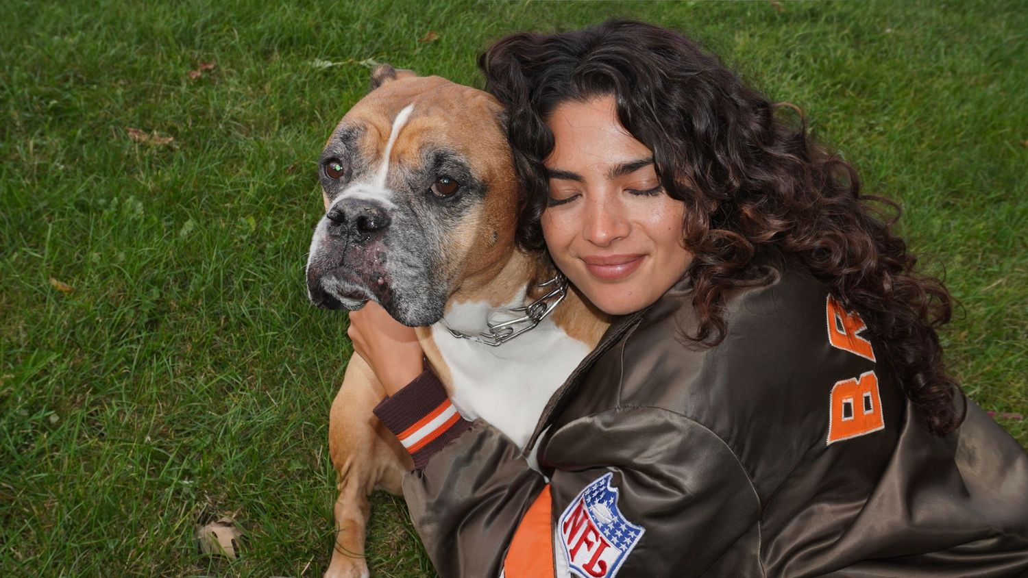 A dog and person share a heartwarming moment together on green grass during a sunny day outdoors.