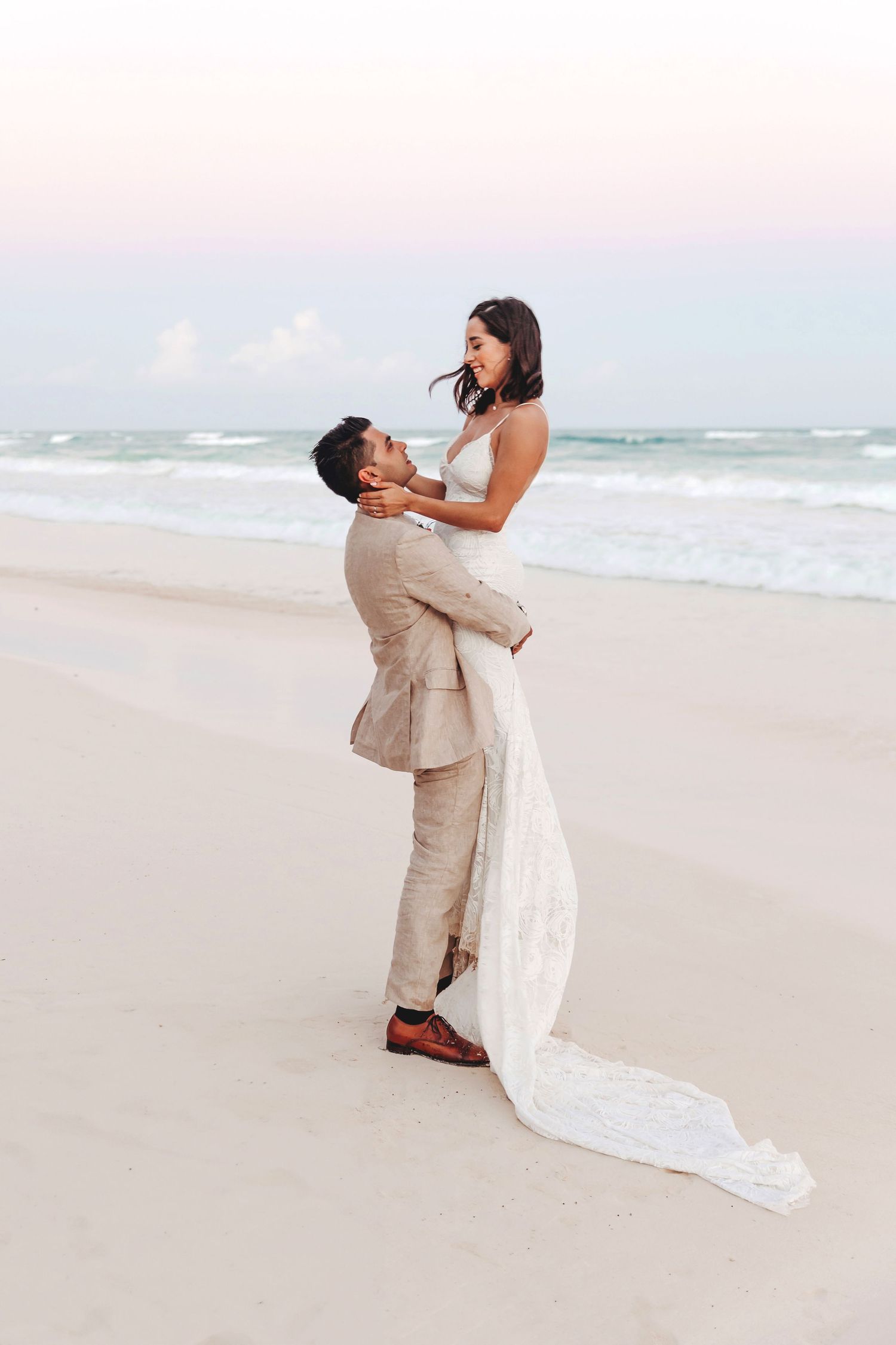 Casa Malca Tulum wedding. Groom lifts bride on white sand beach, turquoise sea & pastel sunset. Captured by Tulum wedding photographer.