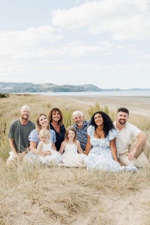 Multi-generational family portrait on sandy beach dunes with coastal scenery, smiling group of eight including children.
