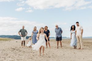 Family group smiling on sandy beach with a young girl in white dress twirling in the foreground.
