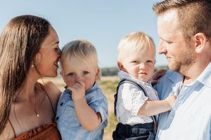 A young family with two blonde toddlers enjoying a sunny outdoor day, parents smiling lovingly at their children.
