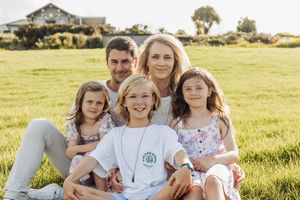 Happy family of five smiling together on green grass field during golden hour outdoor portrait.