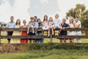 Large multigenerational family posing together along a wooden fence outdoors on a sunny day.