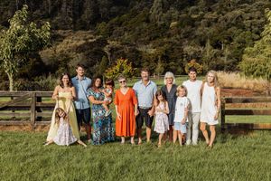 Large family group portrait outdoors on green grass with wooden fence and lush trees in warm golden light.