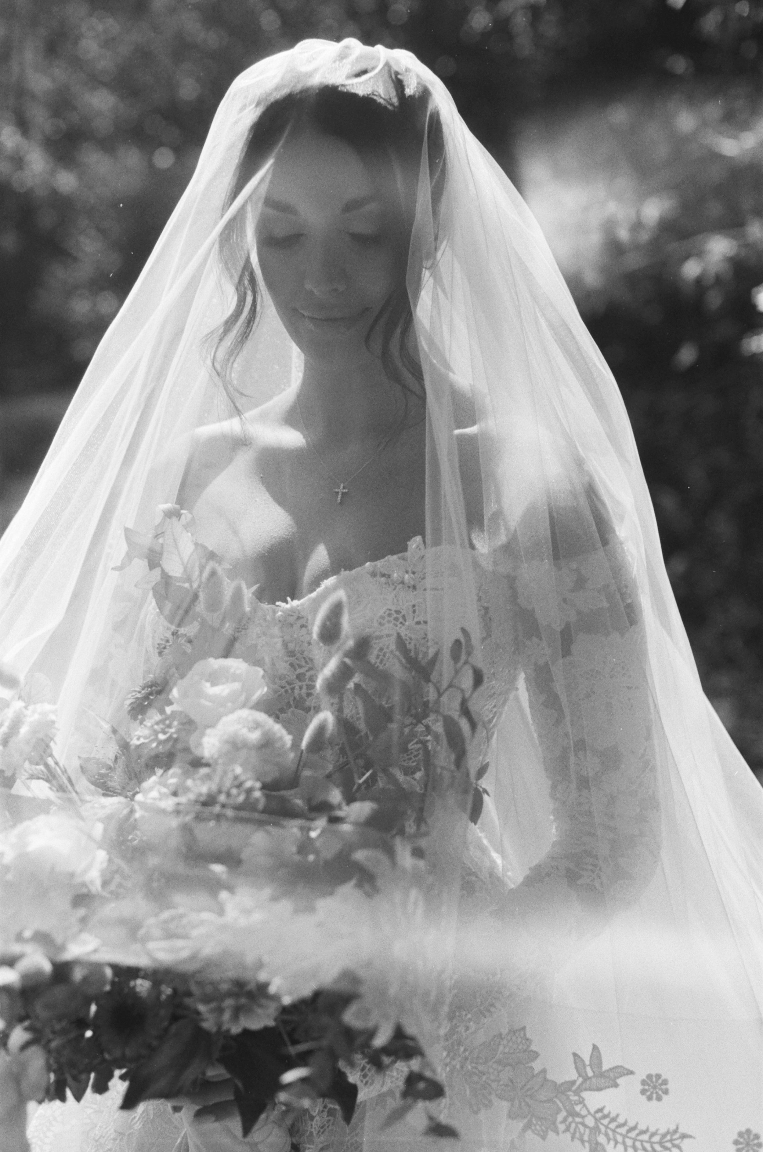 A dreamy black and white photograph of a bride in a veil holding a bouquet with soft lighting and bokeh effect.