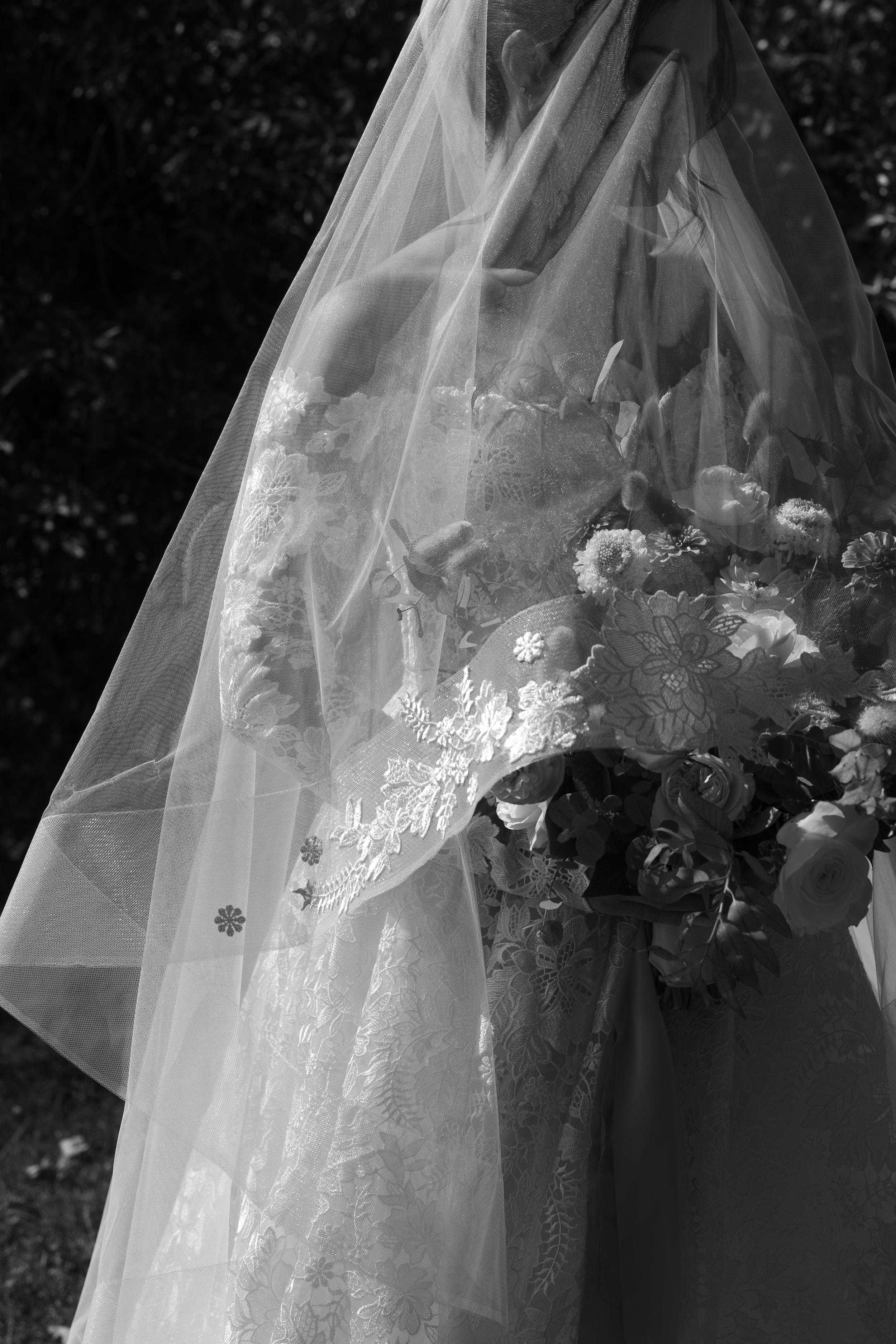 A delicate wedding veil adorned with floral lace details flows gracefully in monochrome black and white photography.