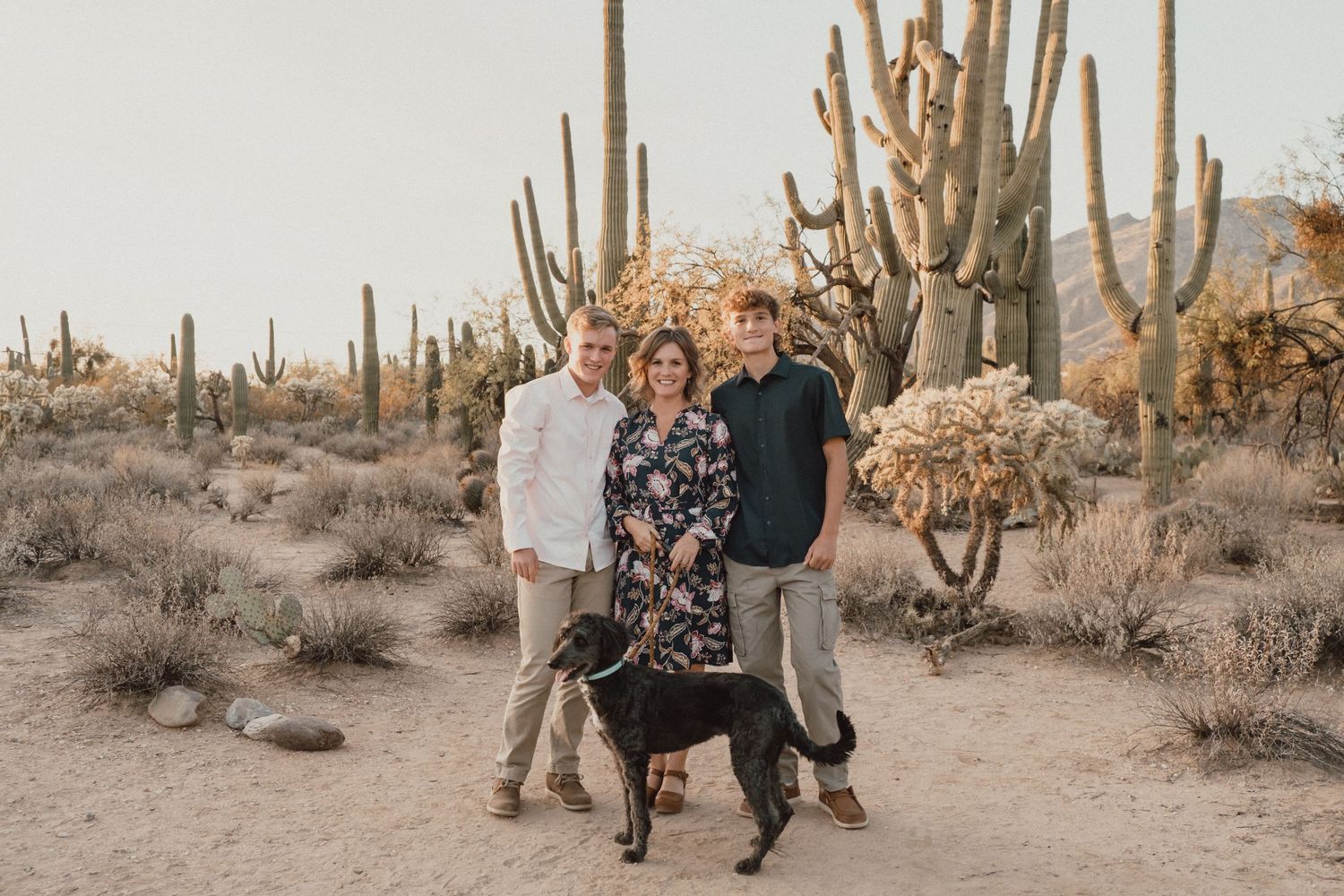 Family portrait with their dog in front of towering saguaro cacti in the Arizona desert.