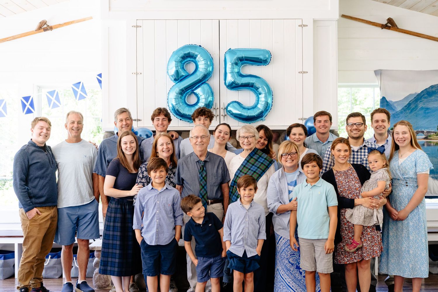 A group celebrates a milestone 85th birthday party with blue number balloons and festive decorations.