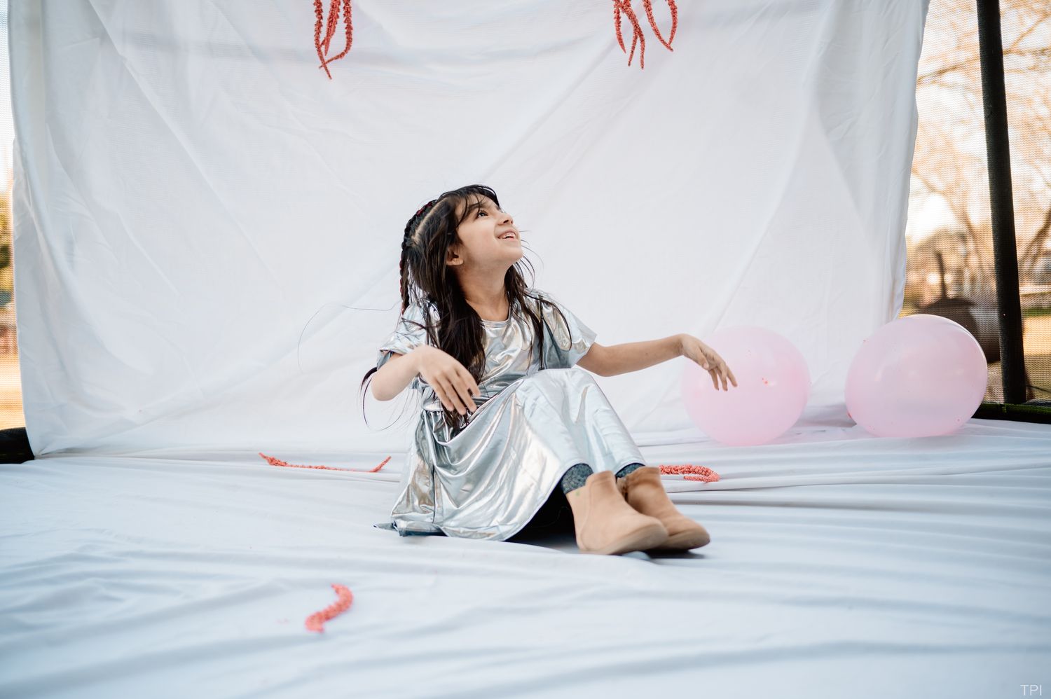 Person in silver dress poses playfully on white backdrop with pink balloons.