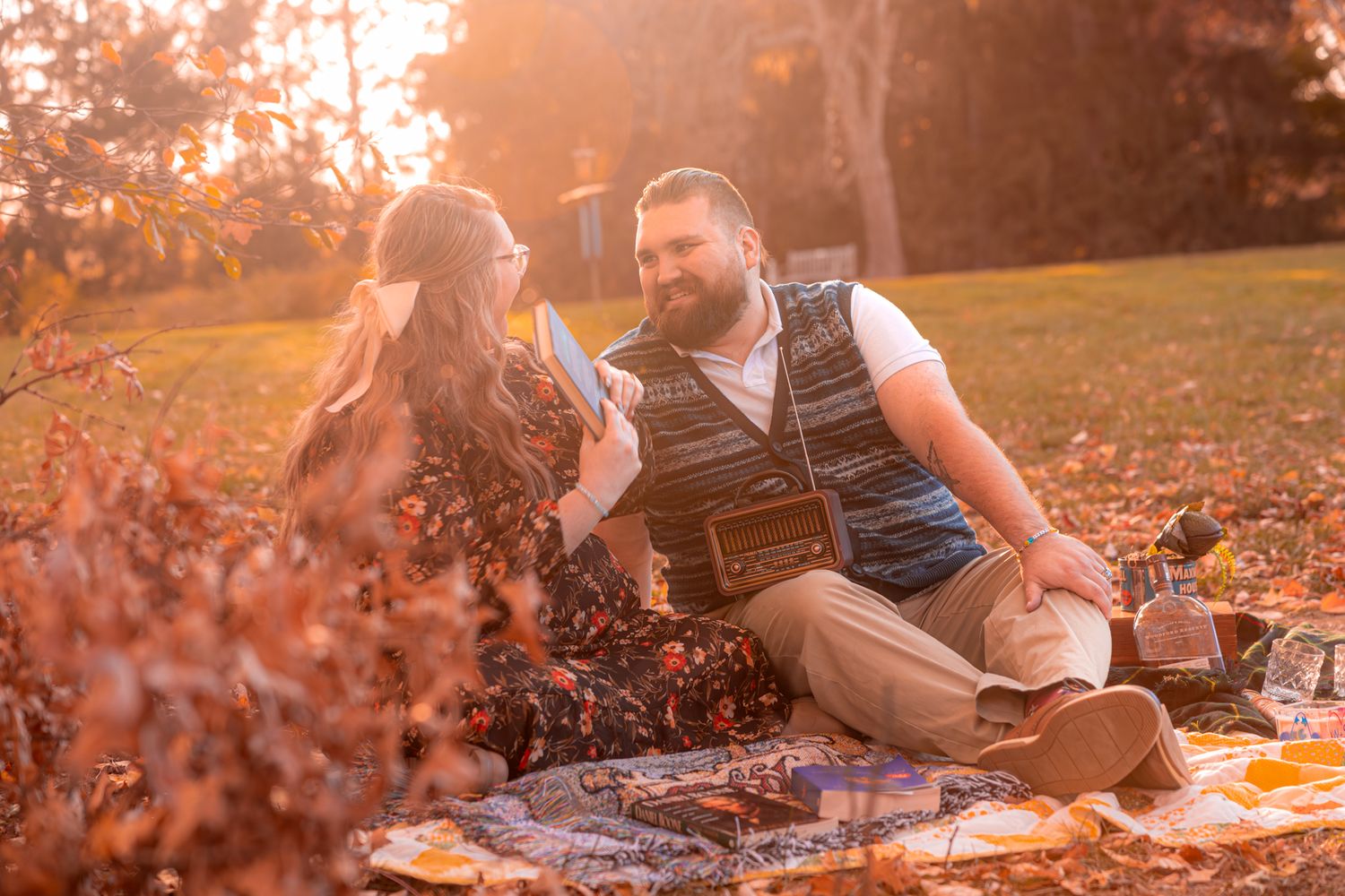 A couple enjoys a romantic autumn picnic on a blanket surrounded by fallen leaves at sunset.