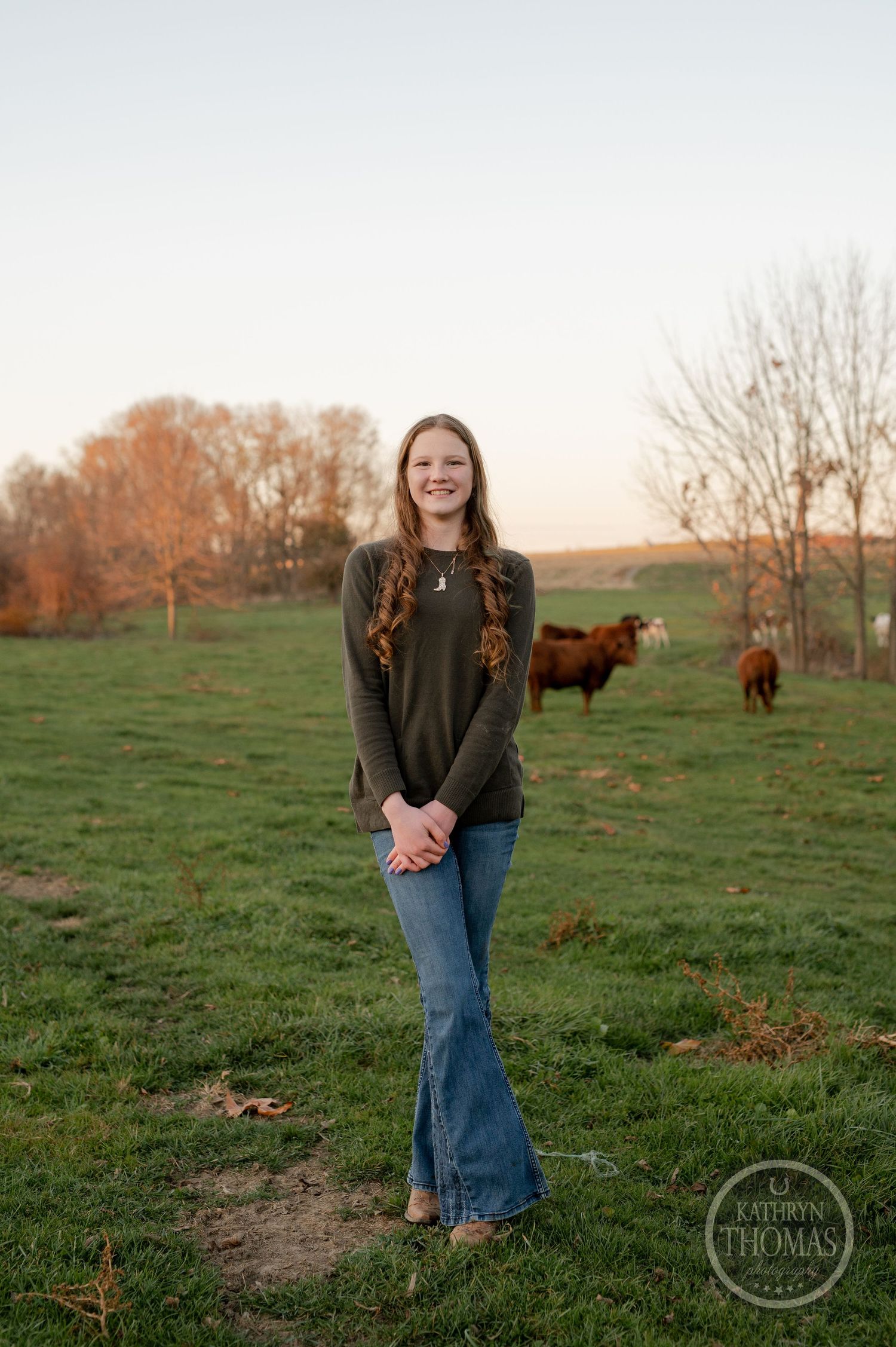 A casual outdoor portrait against a pastoral backdrop with Highland cattle grazing in the distance.