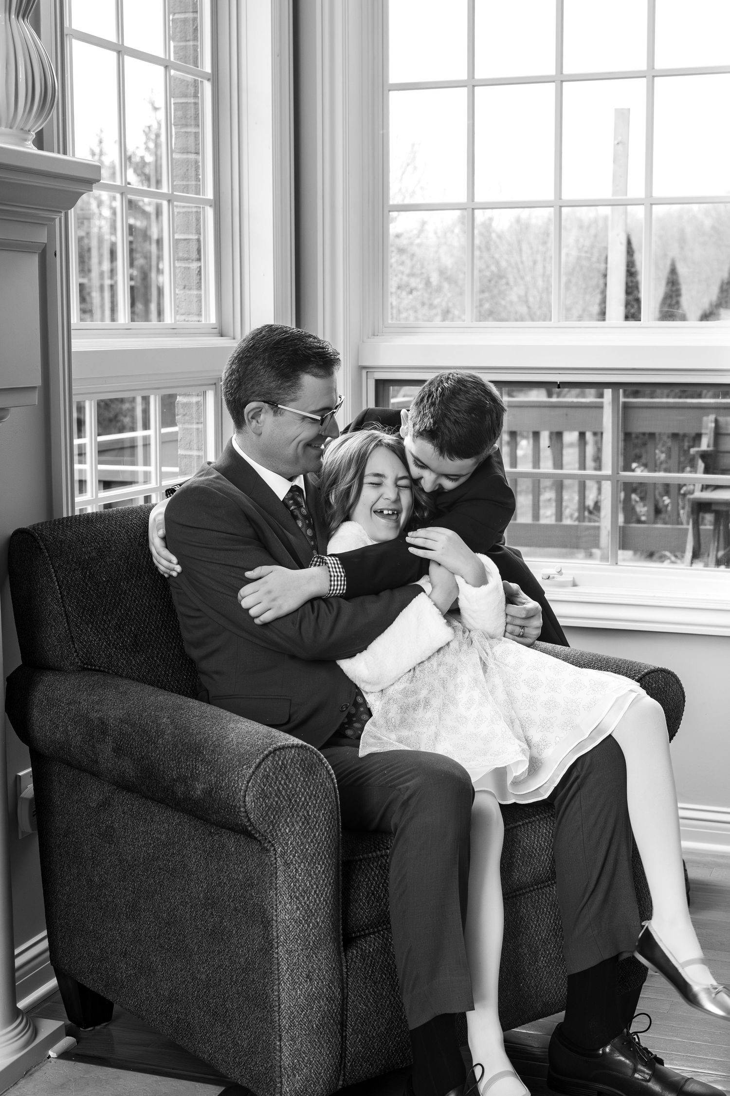 Black and white photo of a tender family moment captured by a window in an armchair. Grand Rapids, Michigan.