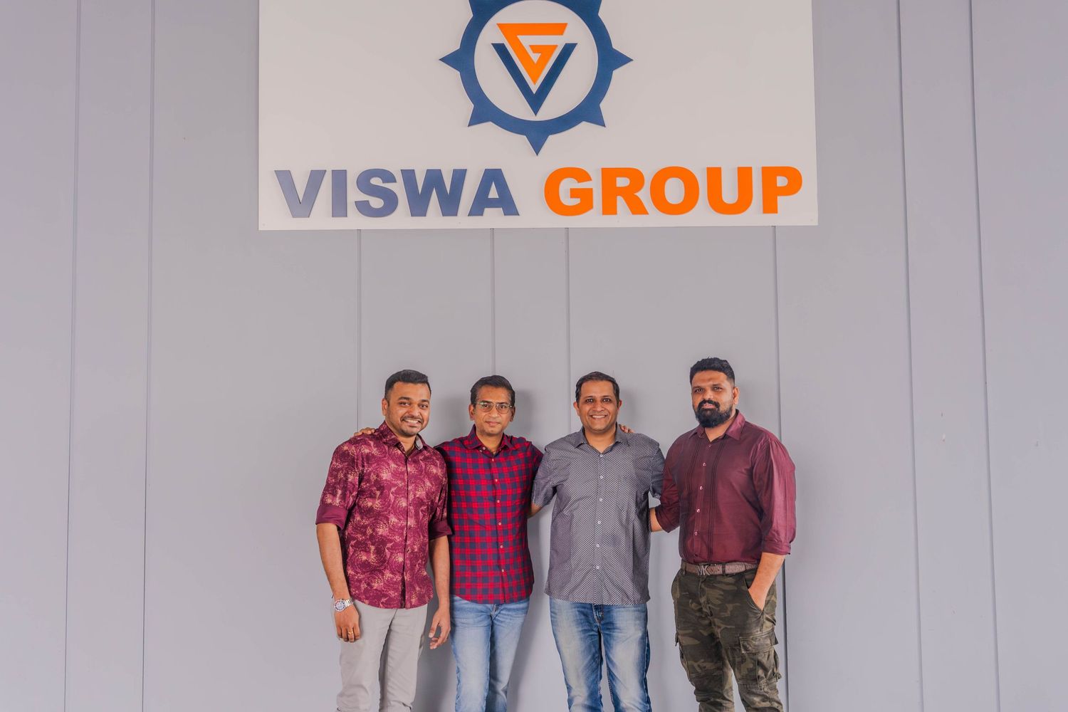 Four staff members standing against a wall with the Viswa Group company logo.