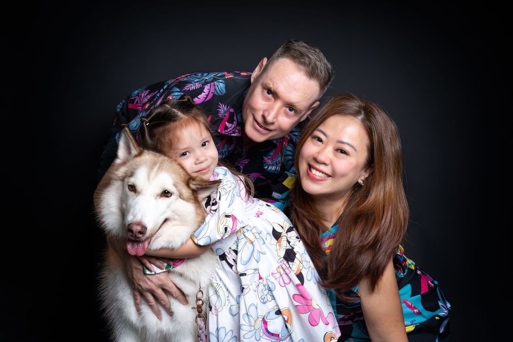 Family portrait featuring a smiling white fluffy dog with a colorful backdrop in studio lighting.