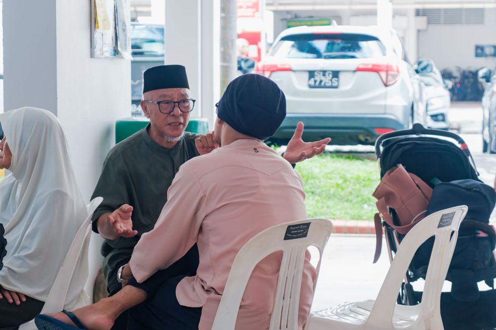 A group in traditional attire engaged in conversation while seated in white chairs outdoors.