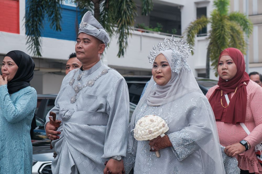 Guests and newlyweds in traditional Malay attire at an outdoor wedding celebration.