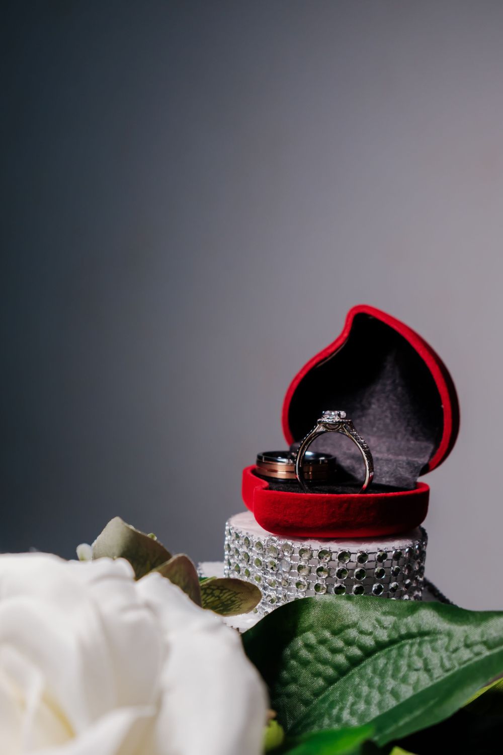 Wedding rings displayed in red heart-shaped box with white rose and greenery.